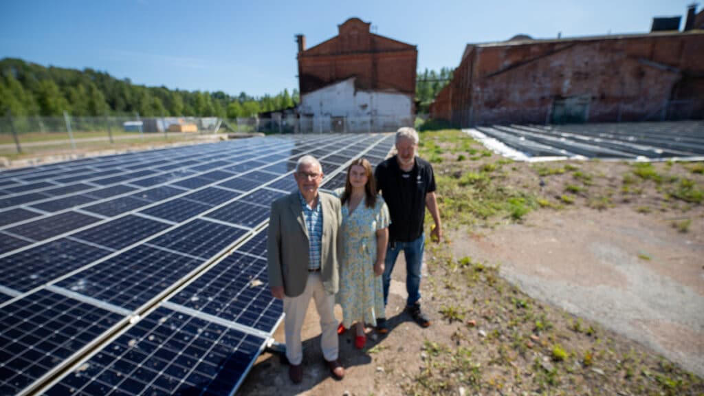Tre personer står bredvid ett gäng marksolceller.