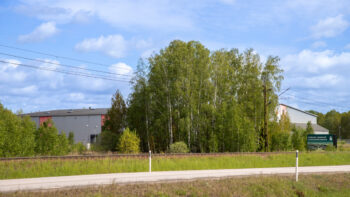 Lagerlokal bakom skogsdunge med järnvägsspår framför.
