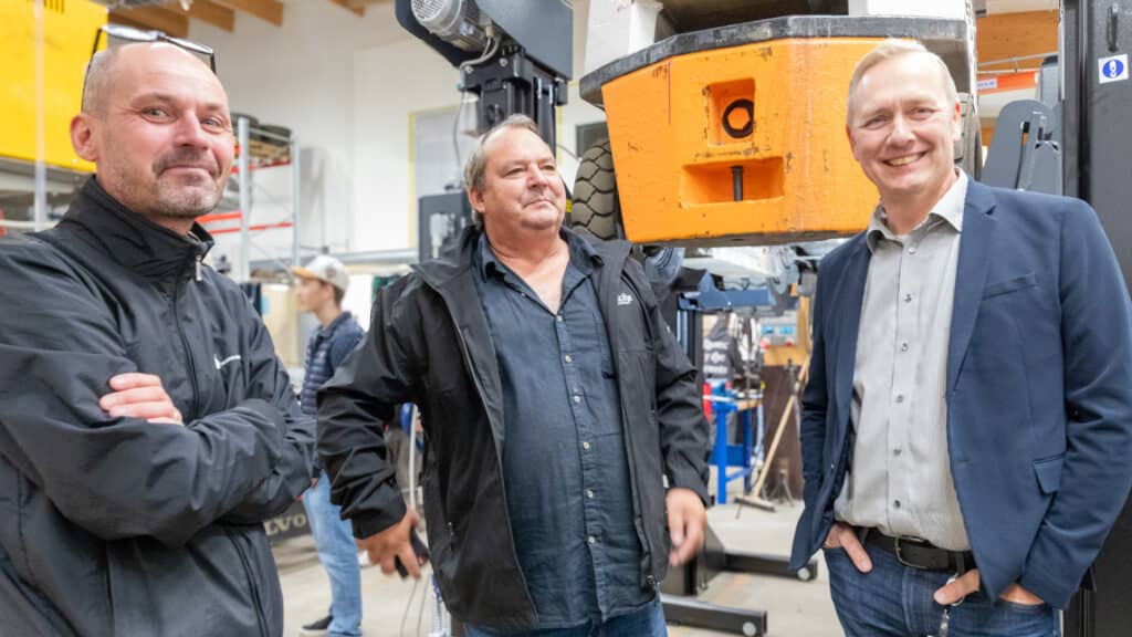 Tre personer står vid en gaffeltruck.