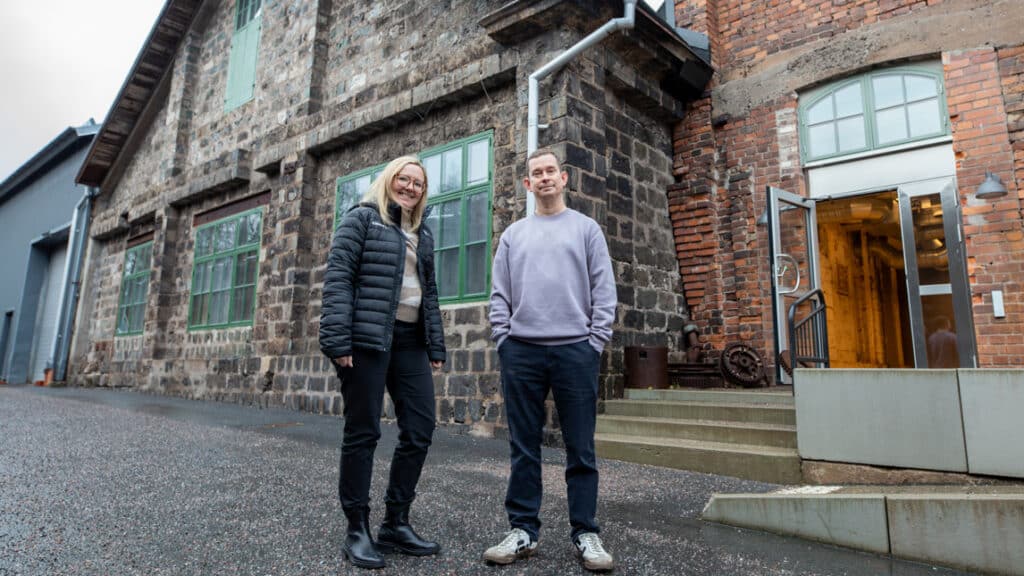 Två personer står utanför en rustik byggnad.