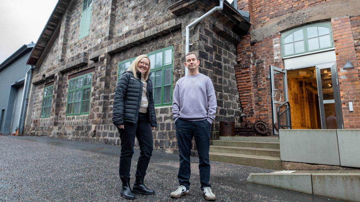 Två personer står utanför en rustik byggnad.